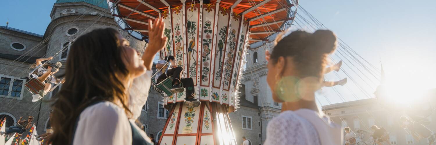 Two women in front of the traditional chain carousel at St. Rupert’s Fair in Salzburg. | © TSG Tourismus Salzburg GmbH / M. Kohlmayr 