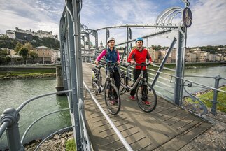 Paar schiebt ihr Rad über den Mozartsteg