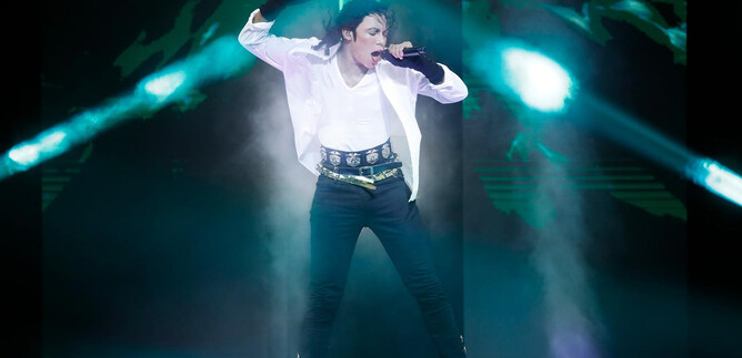 A musician on a stage, energetically singing and dancing. The lights flash in various colors, creating a vibrant atmosphere. | © Franziska Krug_GettyImages