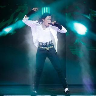 A musician on a stage, energetically singing and dancing. The lights flash in various colors, creating a vibrant atmosphere. | © Franziska Krug_GettyImages