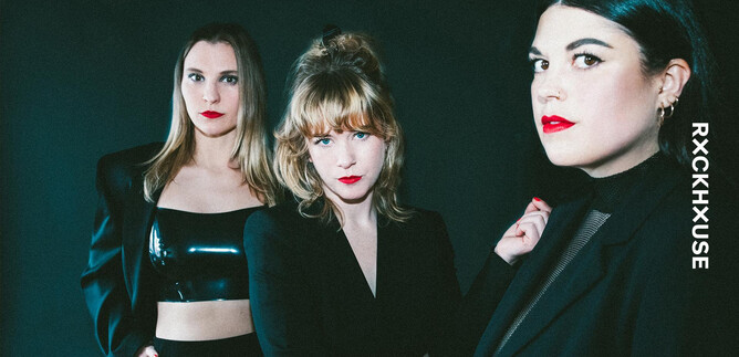 Three women pose in elegant clothing against a dark background. They have a strong gaze and wear bold lipstick. | © Maren Michaelis