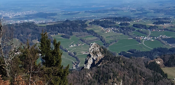 A picturesque landscape with green fields and mountains. In the foreground, a prominent rock is visible. | © Sylvia Wienerroither