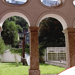 A courtyard with large arches and green grass. In the background, trees and a greenhouse can be seen. | © Kultur Tourismus