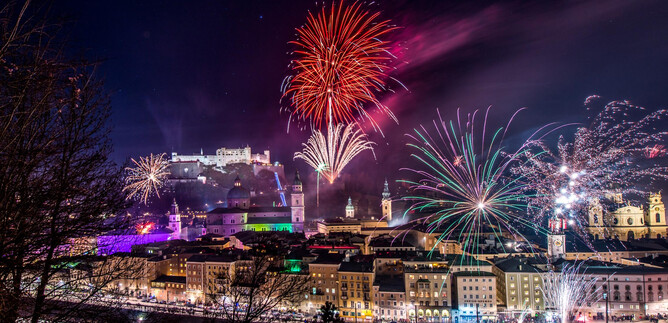 Ein beeindruckendes Feuerwerk erleuchtet den Nachthimmel über einer Stadt. Im Hintergrund ist eine Burg zu sehen, die festlich beleuchtet ist. | © TSG Tourismus Salzburg GmbH_G. Breitegger