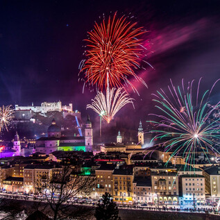 Ein beeindruckendes Feuerwerk erleuchtet den Nachthimmel über einer Stadt. Im Hintergrund ist eine Burg zu sehen, die festlich beleuchtet ist. | © TSG Tourismus Salzburg GmbH_G. Breitegger