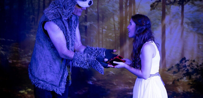 A man in a bear costume hands a woman in a white dress a red object. The scene takes place in a mystical forest. | © Theater mit Seele