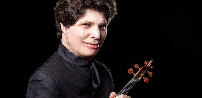 A musician with a violin stands in front of a black background. He smiles kindly and is wearing an elegant suit. | © Suxiao Yang