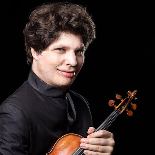 A musician with a violin stands in front of a black background. He smiles kindly and is wearing an elegant suit. | © Suxiao Yang