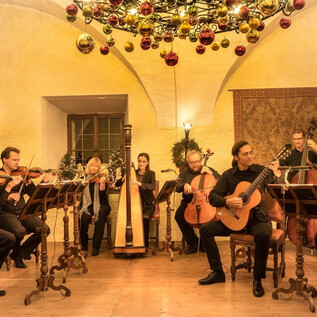 A group of musicians is playing in a festively decorated room. The room is adorned with Christmas ornaments and conveys a cozy atmosphere. | © Salzburg Highlights