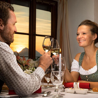 Romantyczna kolacja przy zachodzie słońca. Para wznosi toast swoimi kieliszkami i cieszy się przytulną atmosferą. | © Salzburg Highlights