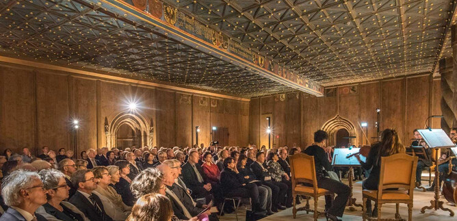 A concert hall with a large audience watching musicians on stage. The atmosphere is festive, and the acoustics are likely excellent. | © Salzburg Highlights