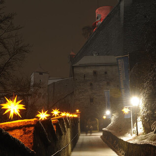 A festively illuminated castle at night, surrounded by snow. Glowing stars decorate the path to the castle. | © Salzburger Burgen und Schlösser
