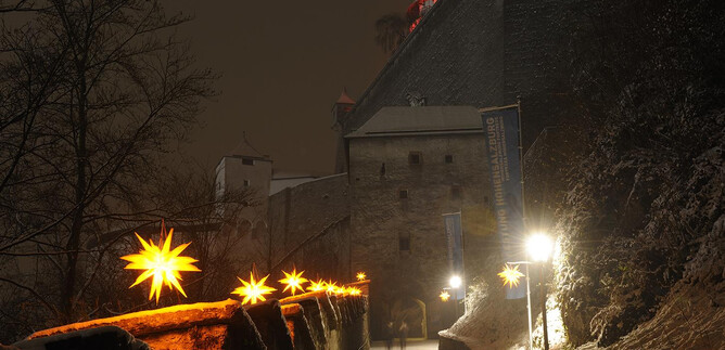 A castle at night, surrounded by snow.  
Glowing stars adorn the path to the castle. | © Salzburger Burgen und Schlösser