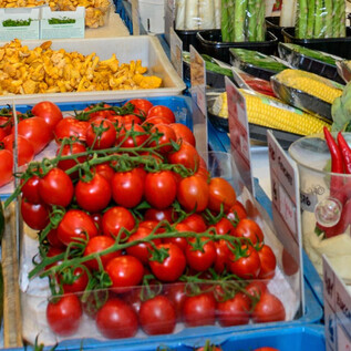 A colorful market with fresh vegetables and fruits. In the foreground are red tomatoes, zucchini, and green bell peppers. | © Tourismus Salzburg GmbH, Breitegger G.