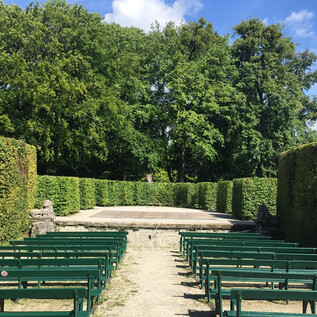 An open-air stage surrounded by tall hedges and benches. The sky is clear and the surroundings feel inviting. | © Tourismus Salzburg