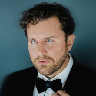 A man in an elegant suit with a black bow tie. He has a serious expression and looks contemplatively into the distance. | © Marco Borelli