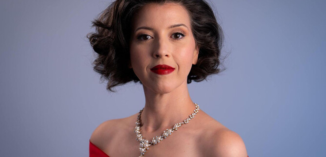An elegant woman in a red evening gown with beautiful jewelry. She has curly hair and is wearing red lipstick. | © Steven Harris