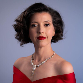 An elegant woman in a red evening gown with beautiful jewelry. She has curly hair and is wearing red lipstick. | © Steven Harris