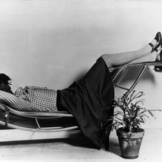 A woman relaxes on a modern lounge chair. Next to her is a pot with a plant. | © Archives Charlotte Perriand / FLC, Bildrecht Wien, 2026