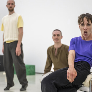 Four dancers are standing in a bright room. The focus is on a dance pose of a woman in a blue shirt. | © Bernhard Müller