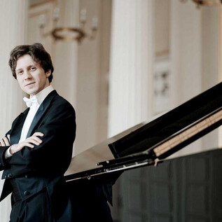 A musician in an elegant suit stands next to a grand piano. He has his arms crossed and is looking directly at the camera. | © Marco Borggreve
