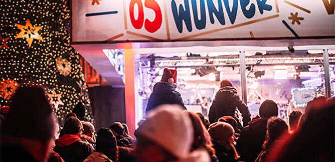 A festive Christmas market scene with many people. In the background, there stands a beautifully decorated Christmas tree and a colorful booth with the sign "Christmas Miracle." | © Martin Krachler_oe3.orf.at