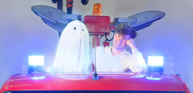 A man is sitting in a vehicle next to a ghostly, white spirit. Blue lights and smoke can be seen in the background. | © SLT / Christian Krautzberger