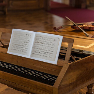 A classic piano with an open sheet of music is in the foreground. In the background, there is a violin on a table. | © DomQuartier Salzburg