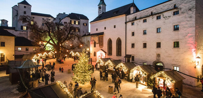 A festive Christmas market with a beautiful tree in the middle. Many people enjoy the atmosphere and the illuminated stalls. | © Festung Hohensalzburg