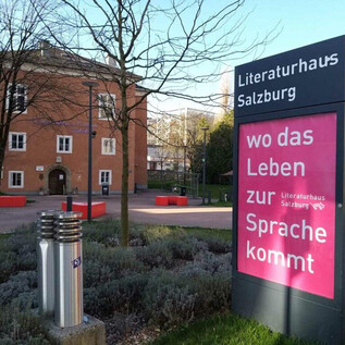 The Literaturhaus Salzburg is a modern building with an inviting outdoor area. Next to the main office, there is an information board with the saying "where life comes to speech." | © Literaturhaus Salzburg