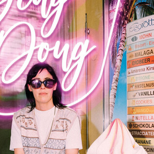 A person is sitting in front of a glowing neon sign with the text "Belly Doug". Next to them is a menu with various ice cream flavors. | © Ingo Pertramer