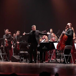 An orchestra is on stage and plays. The conductor directs the musicians, who are dressed in elegant clothes. | © The Showtime Agency GmbH
