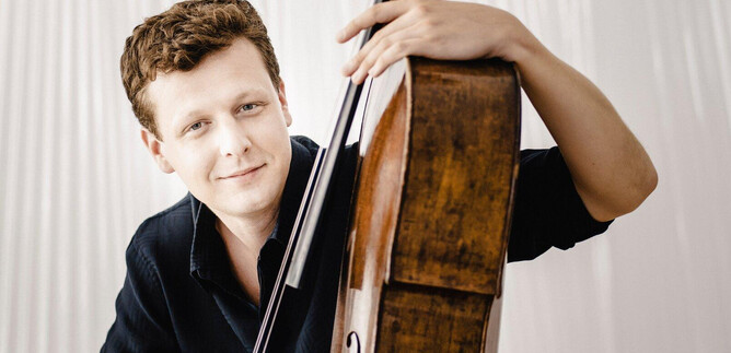 A young man poses with a cello. He has a friendly smile and is wearing a black shirt. | © Marco_Borggreve