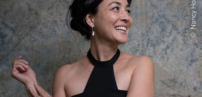 A woman with a joyful smile is wearing a black top. Her gaze is directed upward as she poses elegantly. | © Nancy Horowitz