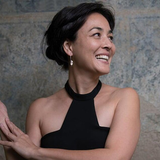 A woman with a joyful smile is wearing a black top. Her gaze is directed upward as she poses elegantly. | © Nancy Horowitz