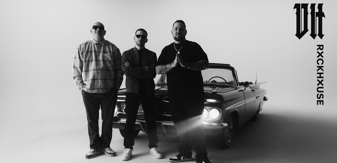 Three men are standing in front of a classic car in a minimalist studio space. The scene is black and white and conveys a strong visual impression. | © Rockhouse Salzburg