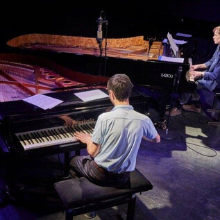 Two pianists are sitting on stage and playing together. One pianist is at a piano, while the other is seated at an additional grand piano. | © Jazzit