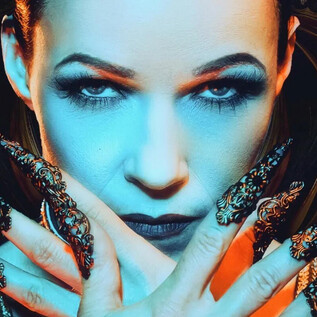 A dramatic portrait featuring a woman with impressive, ornate nails. The background is vibrant and radiates a mystical atmosphere. | © Rockhouse Salzburg