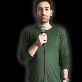 A man with a microphone stands in front of a black background. He is wearing a green shirt and looking at the camera. | © Fabi Rommel