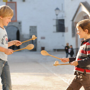 Two boys are playing with wooden spoons in a sunny environment. They are laughing and seem to be having a lot of fun. | © Festung Hohensalzburg