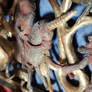 An artistic wooden carving depicts a figure on a unicorn. The background is in shades of blue and gold. | © Salzburger Burgen und Schlösser