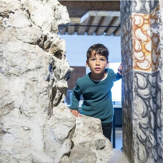 A boy looks curiously through a wall opening. In the background, a bright room can be seen. | © Salzburg Museum