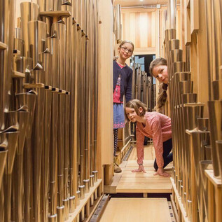 Three children are standing between the pipes of an organ. They are smiling and having a lot of fun exploring. | © Eva trifft