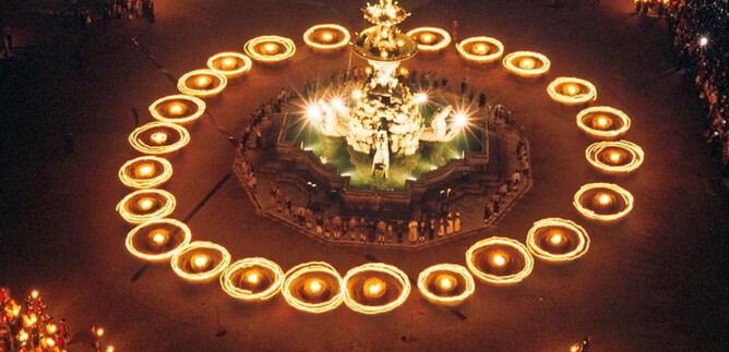 A festive square illuminated by numerous torches surrounding a beautiful fountain. The atmosphere is lively and celebratory, filled with people. | © Land Salzburg, Kulturabteilung