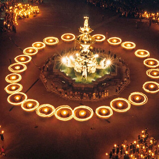 A festive square illuminated by numerous torches surrounding a beautiful fountain. The atmosphere is lively and celebratory, filled with people. | © Land Salzburg, Kulturabteilung