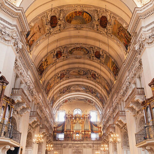 An impressive interior view of the church with high ceilings and elaborate frescoes. Two large organs are placed on the sides, creating a majestic atmosphere. | © Erzdiözese Salzburg