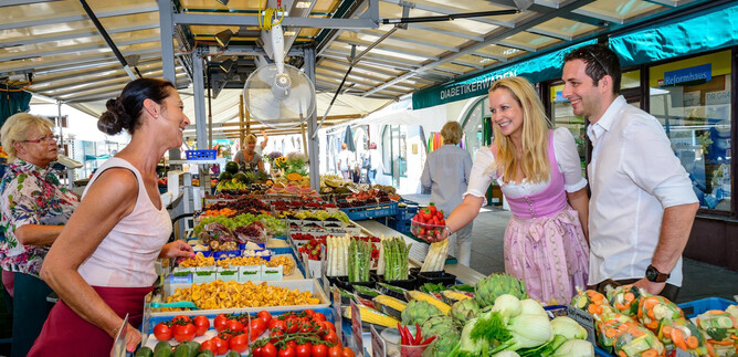 A lively market with fresh fruits and vegetables. Two customers are chatting amicably with a salesperson. | © Tourismus Salzburg GmbH, Breitegger G.