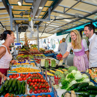 A lively market with fresh fruits and vegetables. Two customers are chatting amicably with a salesperson. | © Tourismus Salzburg GmbH, Breitegger G.