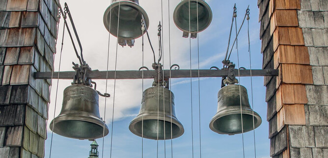 Eine Reihe von Glocken hängt an einem Gerüst, umgeben von einem schönen Himmel. Im Hintergrund ist ein Turm mit einer grünen Kuppel sichtbar. | © SalzburgerLand Tourismus / Eva trifft