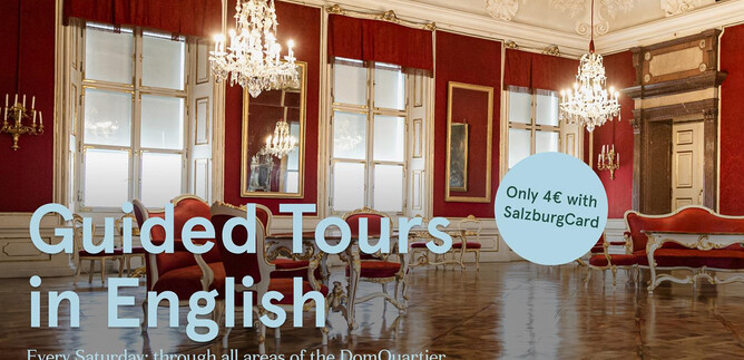 An elegant room with crystal chandeliers and large windows. There is information about guided tours in English at the DomQuartier.